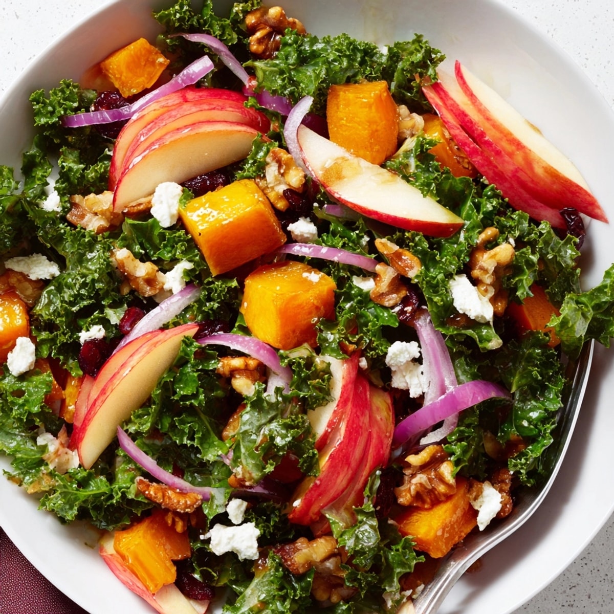 Close-up of a vibrant Harvest Apple Kale Salad with toasted pecans and feta.