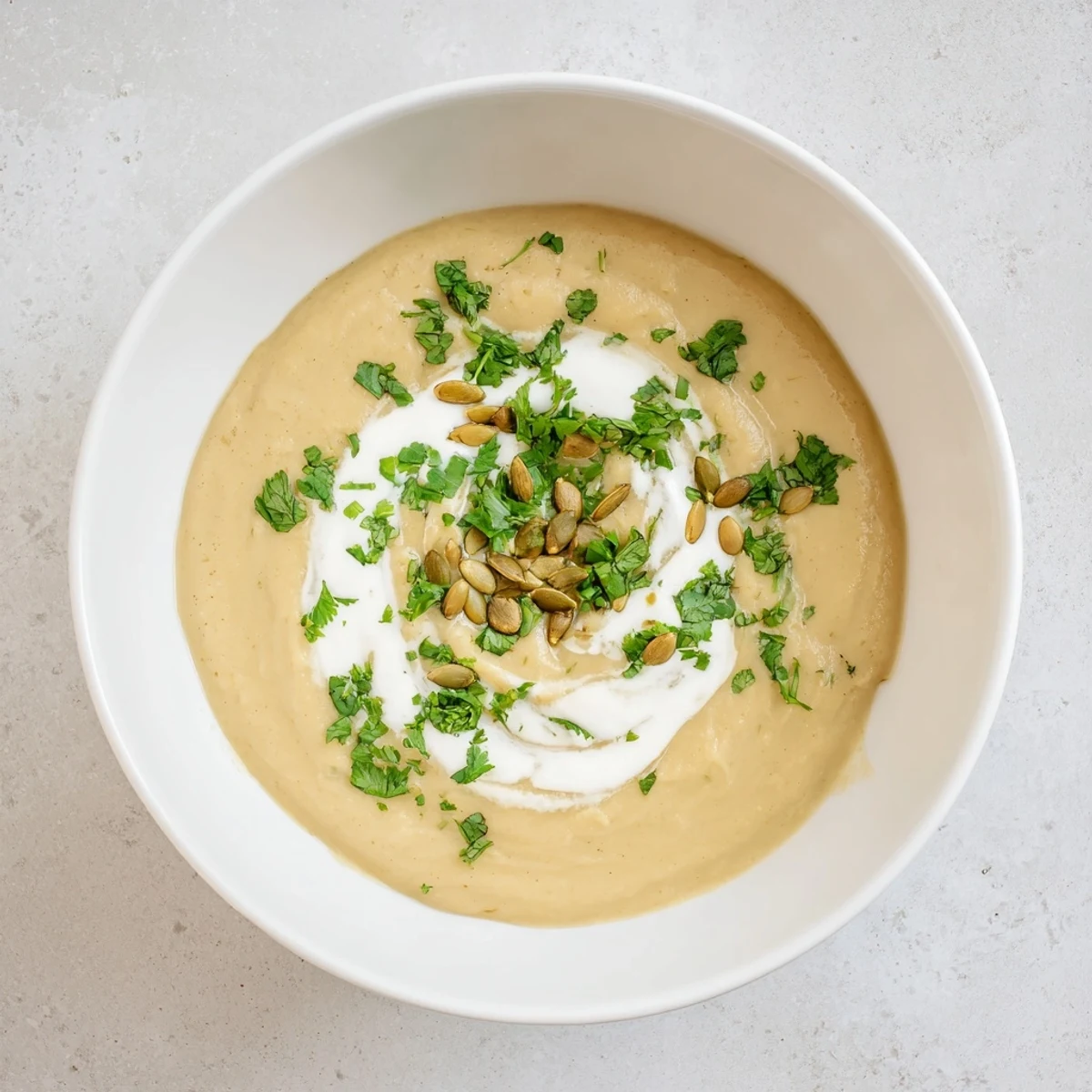 Close-up of a bowl of Spiced Parsnip and Apple Soup, garnished with green herbs and cream.