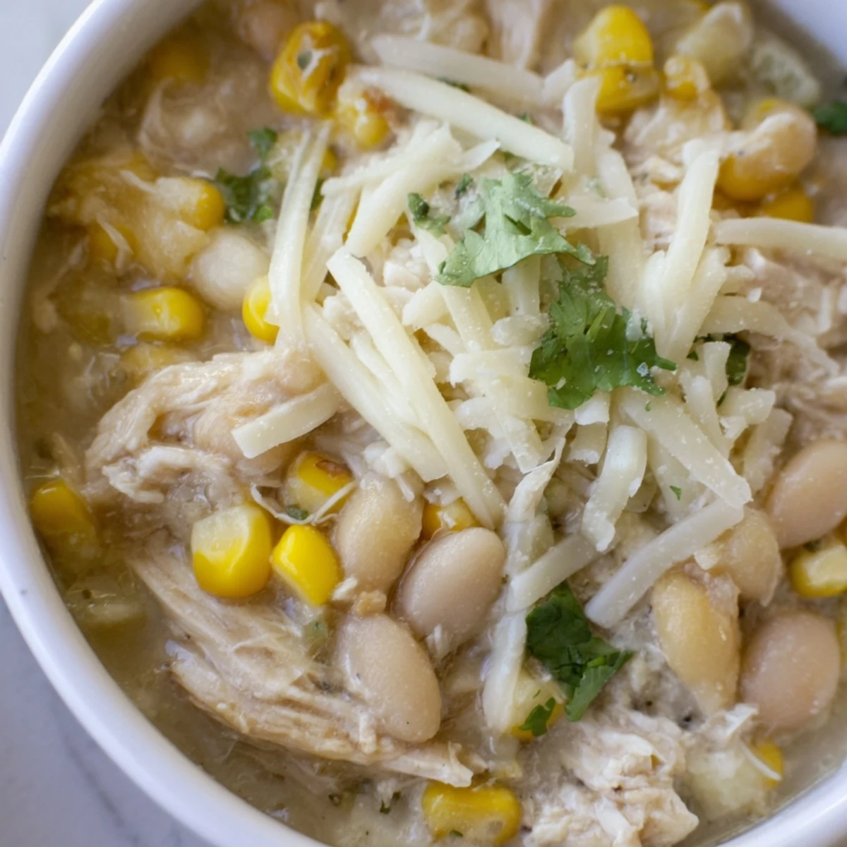 Steaming bowl of Creamy White Chicken Chili topped with cilantro, green onions, and cheese, served with lime wedges and cornbread.