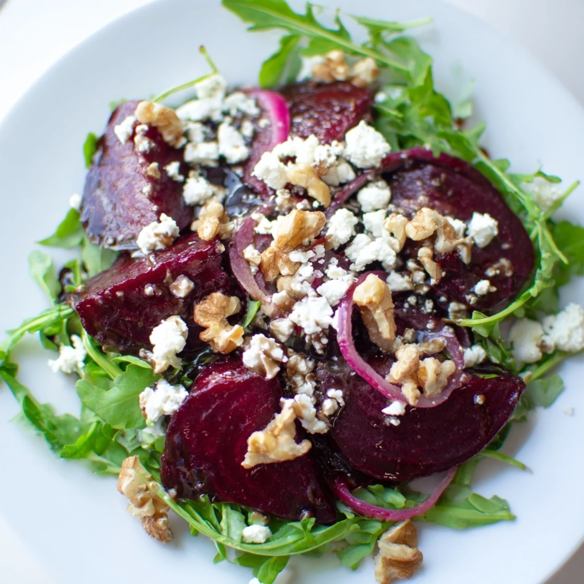 Roasted Beet Salad with Arugula and Feta on a white platter garnished with toasted walnuts and red onion.