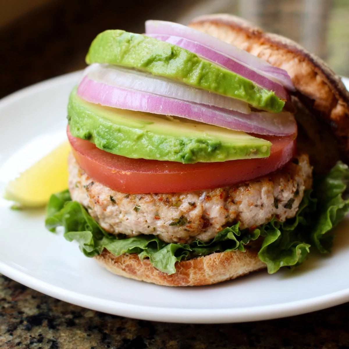 A fully cooked turkey burger with avocado on a toasted whole wheat bun, layered with tomato and crisp lettuce.