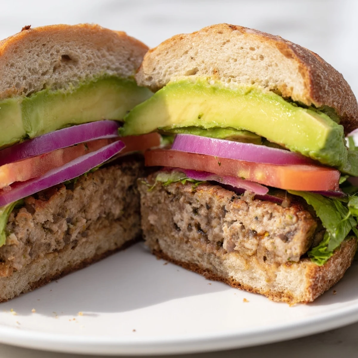 The grilled turkey burger with avocado is topped with red onion and mayo, served on a sesame seed bun.