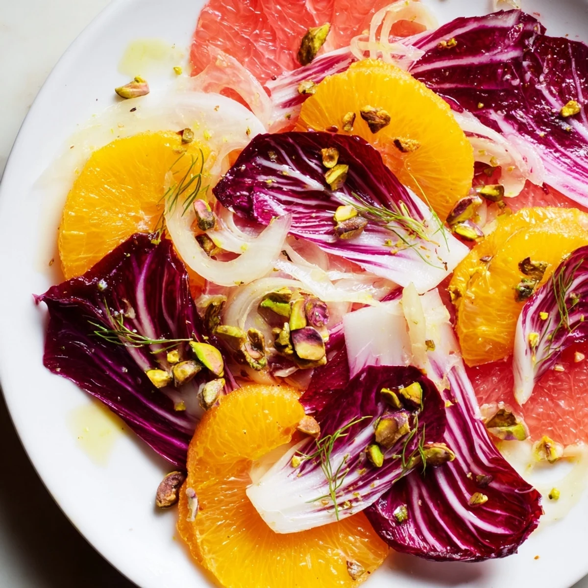 Freshly sliced Winter Citrus Salad with Radicchio and Fennel on a marble counter, topped with toasted pistachios and glistening vinaigrette.