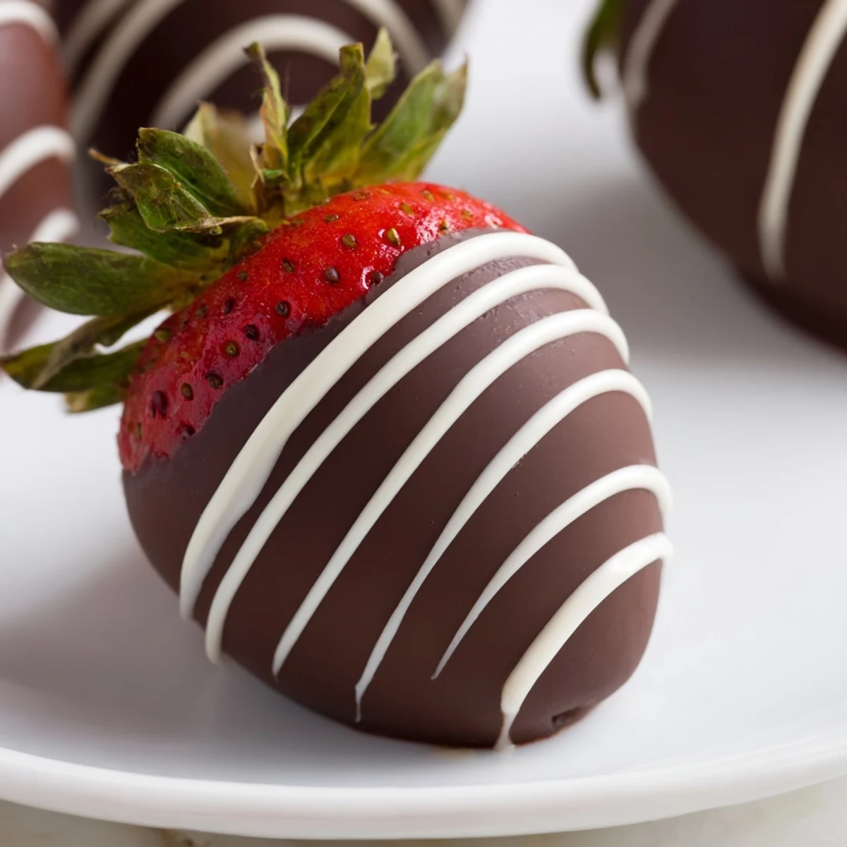 Decadent chocolate dipped strawberries with white chocolate drizzle garnished with pistachios on a serving platter with champagne.