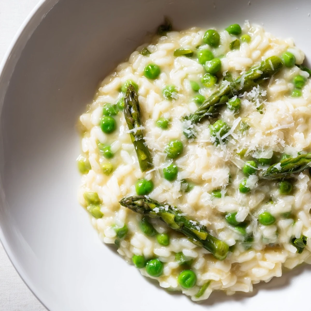 Creamy asparagus and pea risotto in a white bowl, garnished with fresh Parmesan and a sprig of dill.