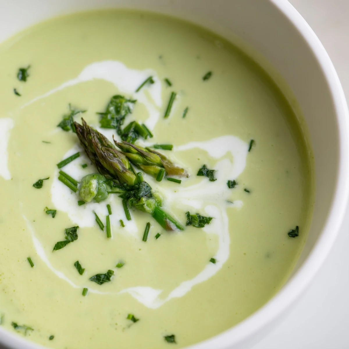 Roasted asparagus and pea soup garnished with fresh herbs and a drizzle of cream in a rustic bowl.