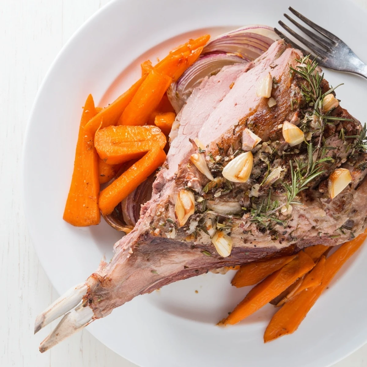 Overhead view of a golden-brown Slow Roasted Leg of Lamb with Garlic and Lemon surrounded by caramelized vegetables and a drizzle of pan jus.