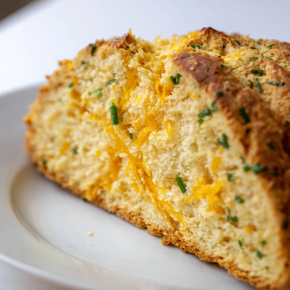 A close-up of Savory Cheddar & Chive Irish Soda Bread, its golden crust speckled with herbs and melted cheese on a rustic cutting board.