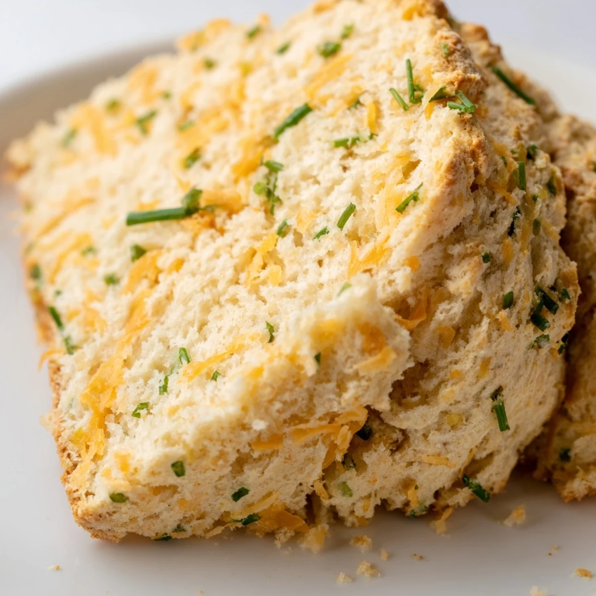 A thick slice of Savory Cheddar & Chive Irish Soda Bread resting on a checkered cloth, perfect for serving with soup or butter.