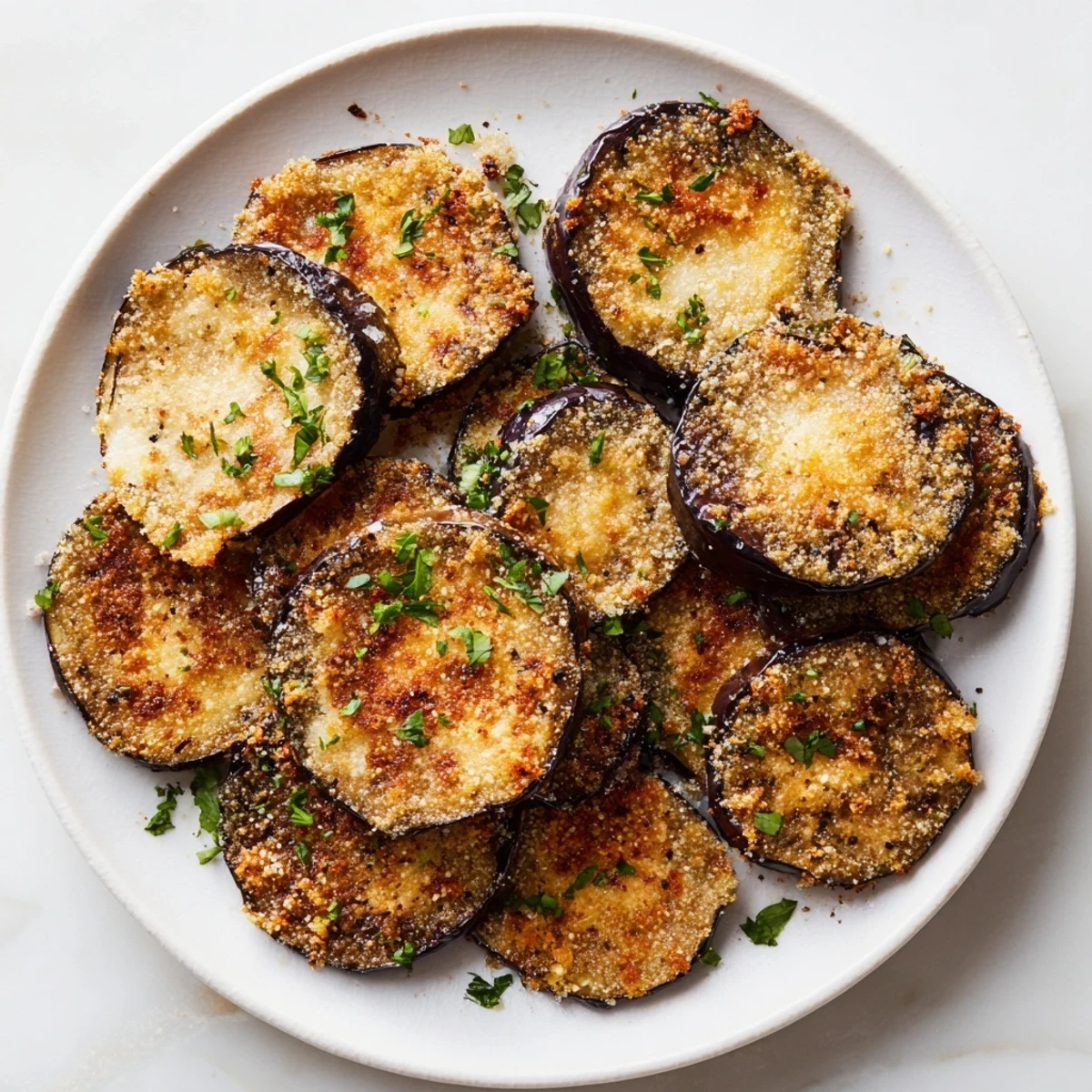 Golden roasted eggplant slices topped with crispy Parmesan and Mediterranean herbs, served as a savory gluten-free appetizer on a white plate.