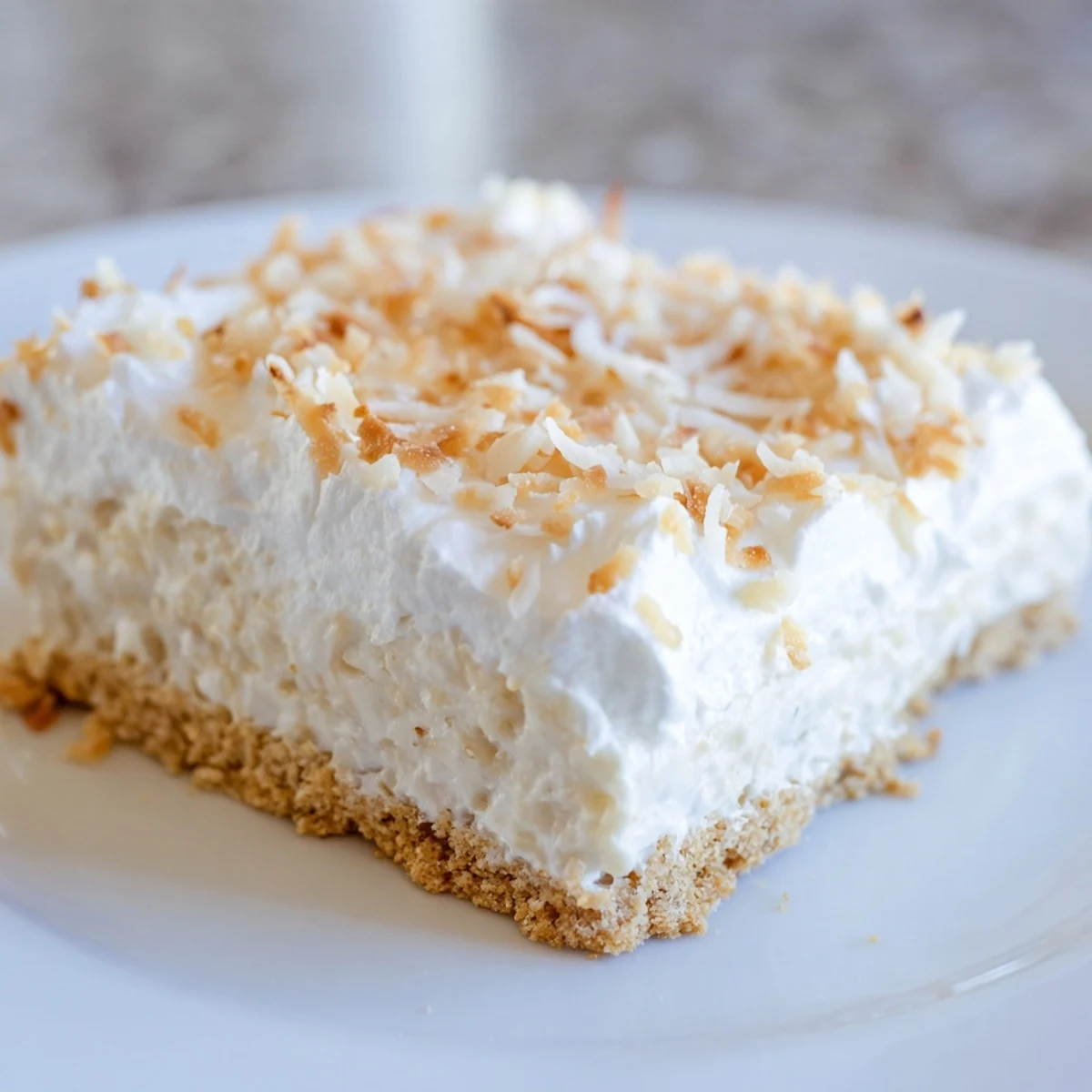 Slice of Coconut Cream Dream Bars on a dessert plate with a drizzle of coconut sauce and a mint leaf garnish.
