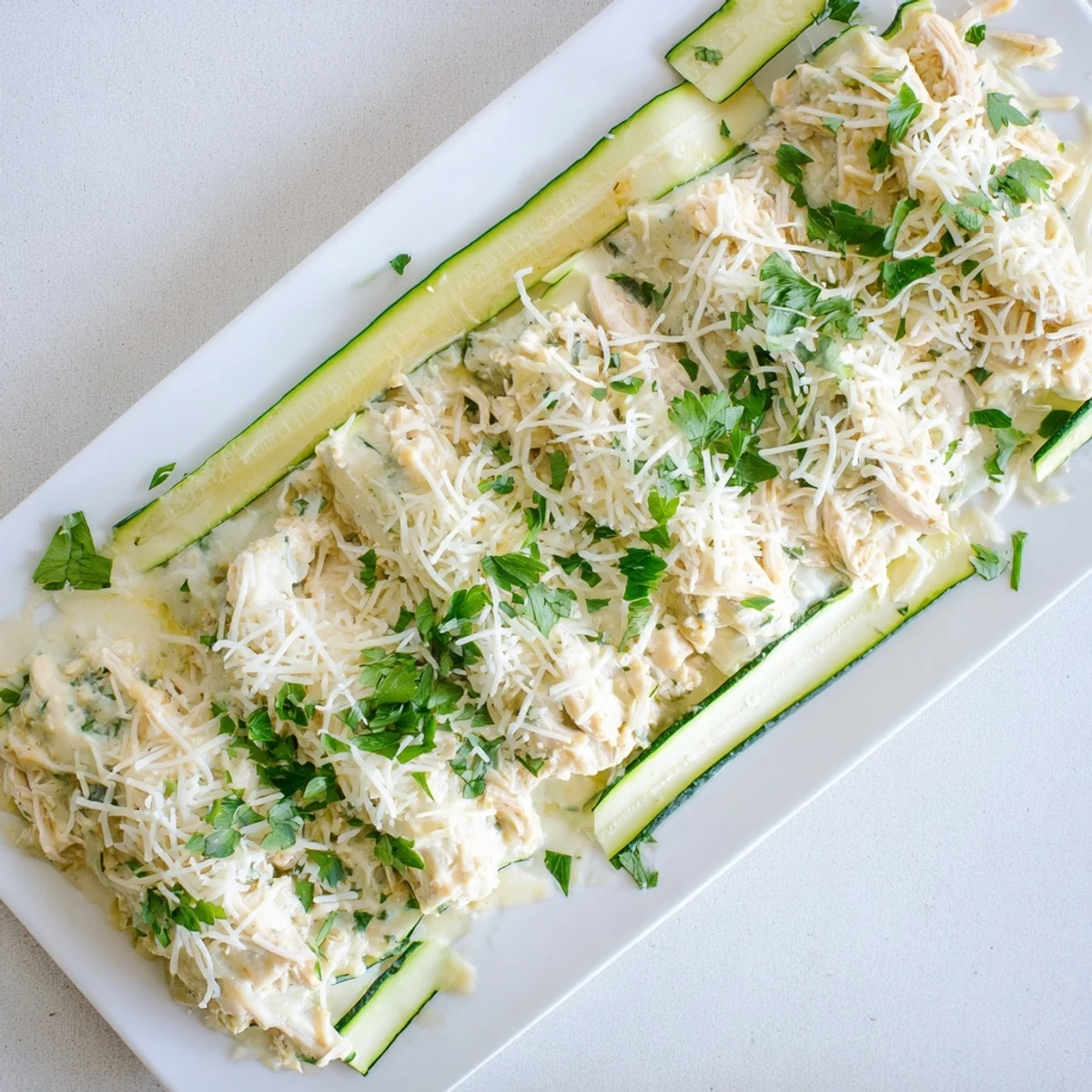 Close-up of creamy Chicken Alfredo Zucchini Lasagna layers on a white ceramic plate.  