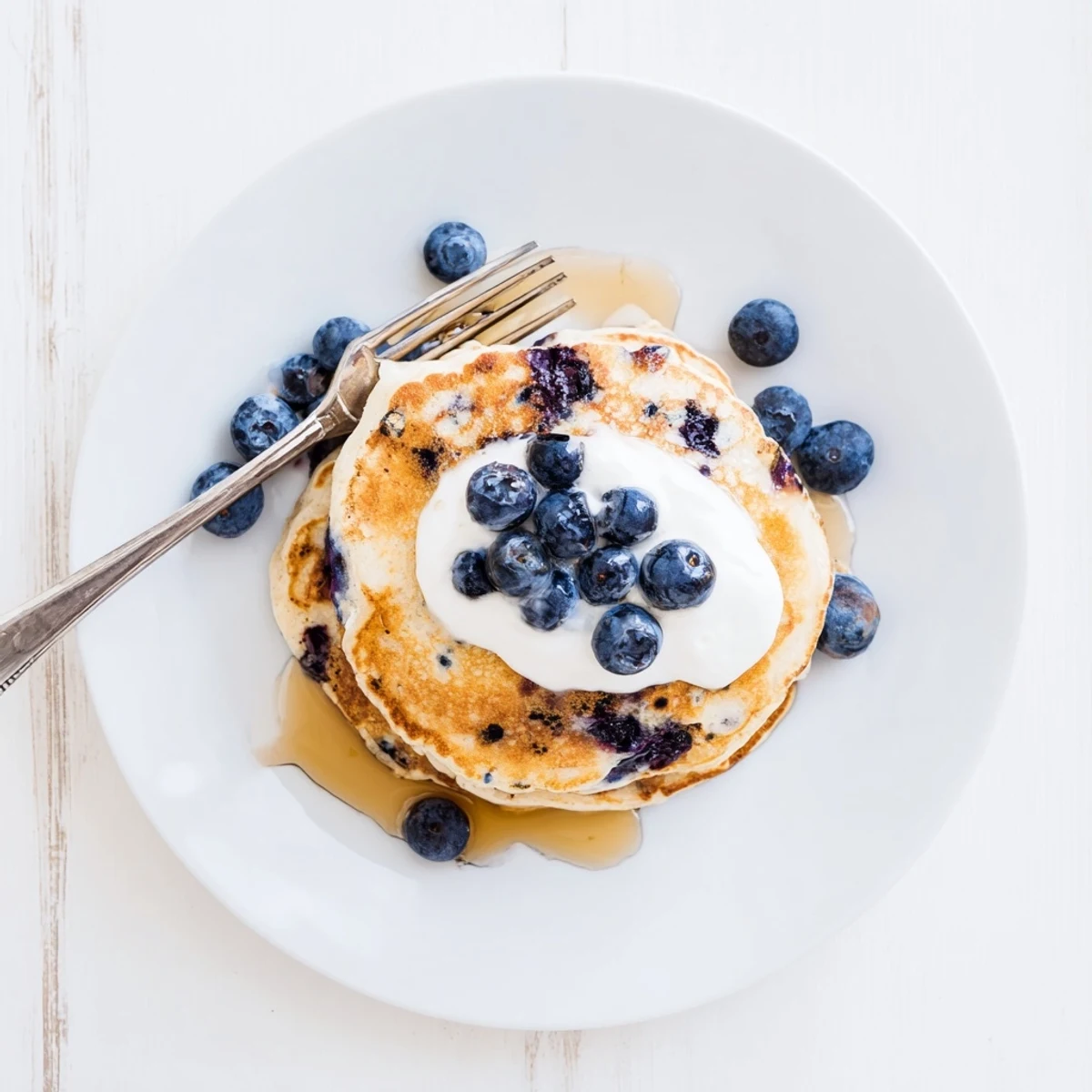 Close-up of Greek Yogurt Blueberry Pancakes revealing juicy berries and a tangy crumb, plated with butter and syrup for breakfast.