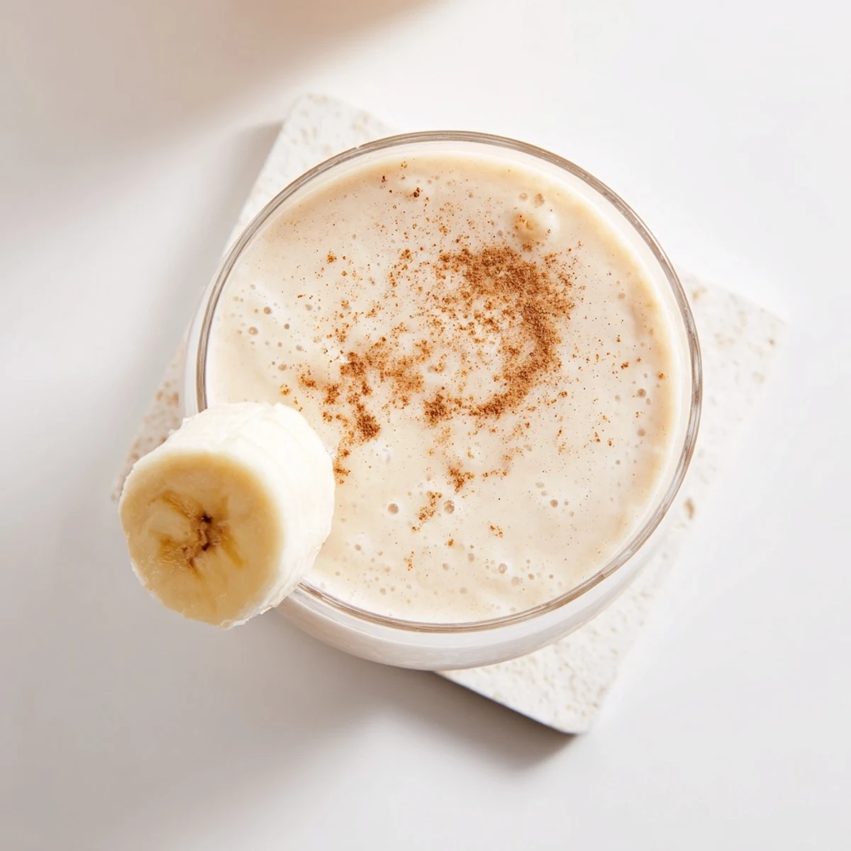 Tall glass filled with creamy Greek yogurt banana smoothie topped with fresh banana slices