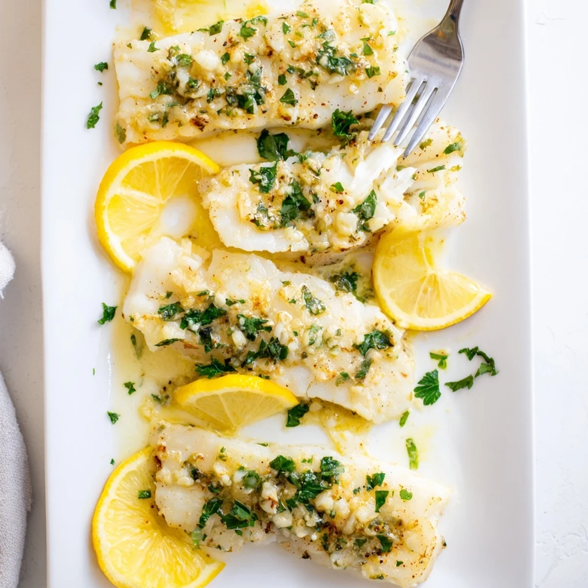 Flaky tender lemon garlic baked cod served with roasted vegetables and lemon wedge garnish