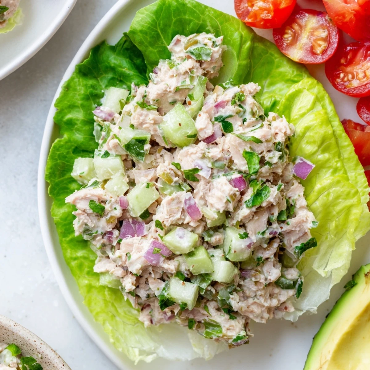 Tuna salad lettuce wraps topped with sliced avocado and cherry tomatoes on white platter