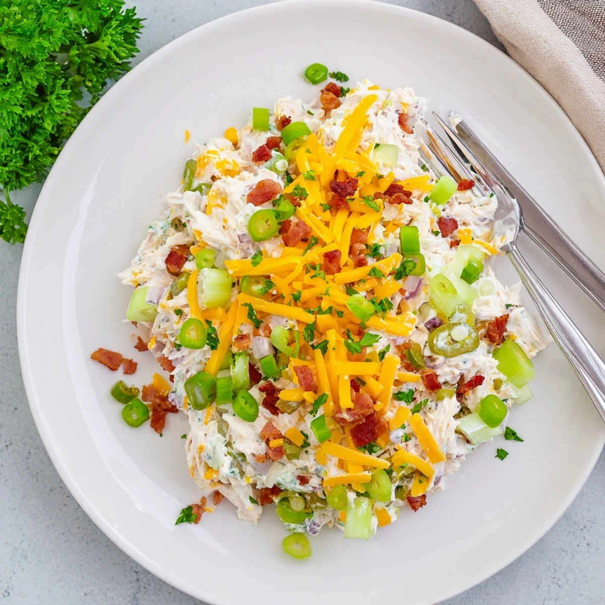 Creamy low carb jalapeño popper cottage cheese chicken salad served in a white bowl with fresh green onions and bacon bits on top