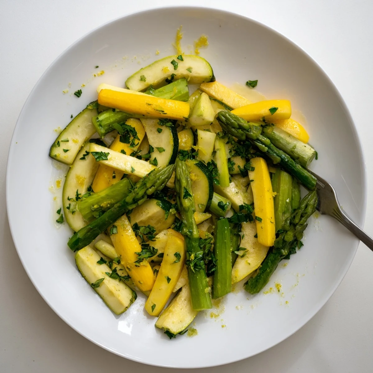 Golden flavorful asparagus with zucchini and squash arranged on a white serving plate with parsley