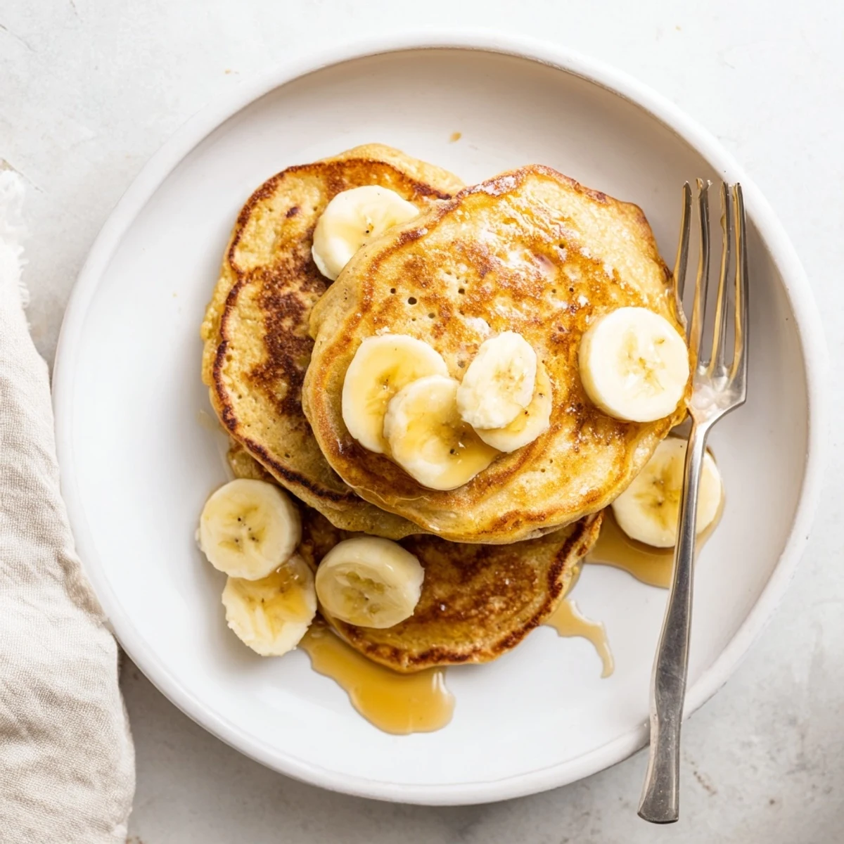 Golden stack of fluffy Greek yogurt banana pancakes drizzled with maple syrup