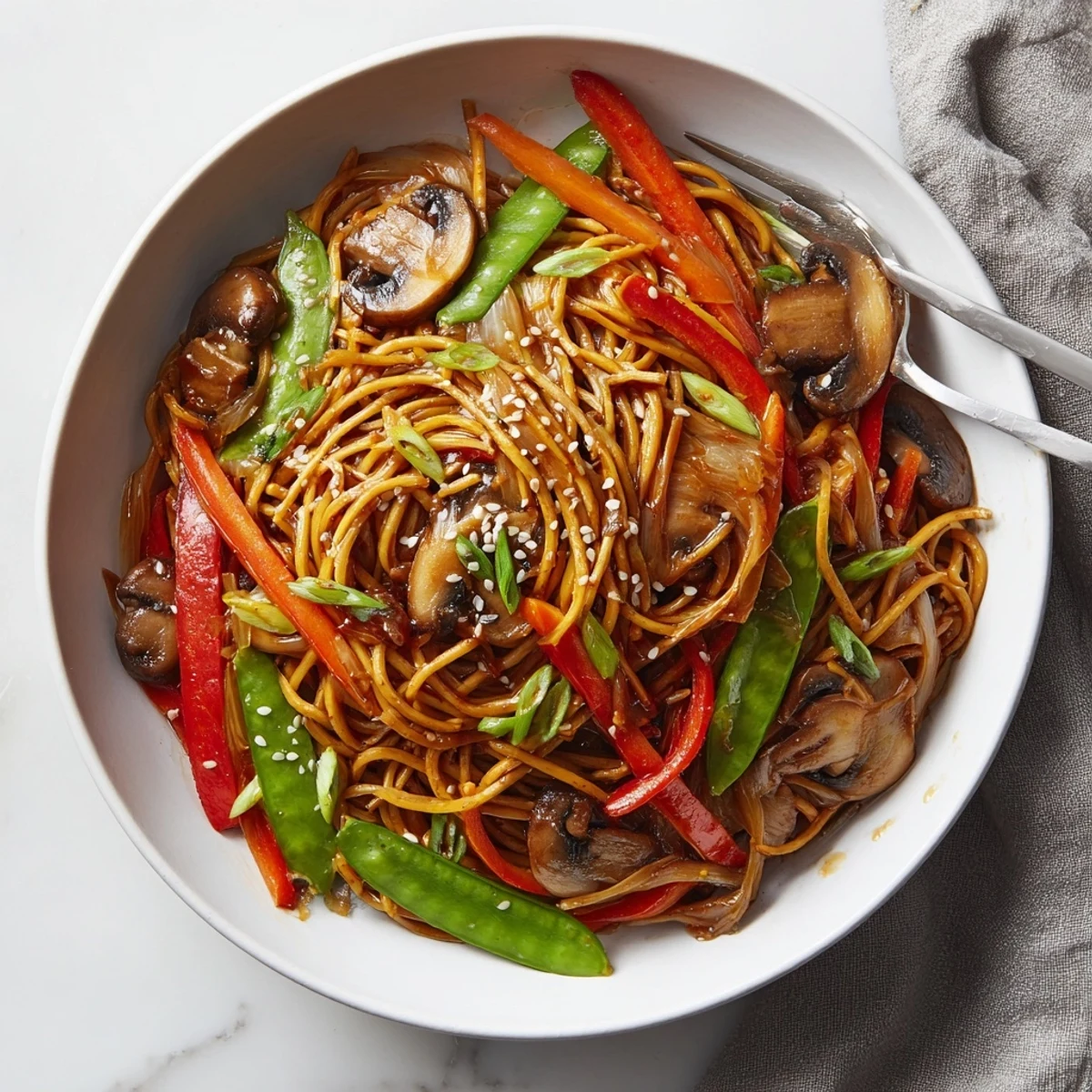 Steamy bowl of vegetarian garlic mushroom chow mein garnished with sesame seeds and fresh green onions