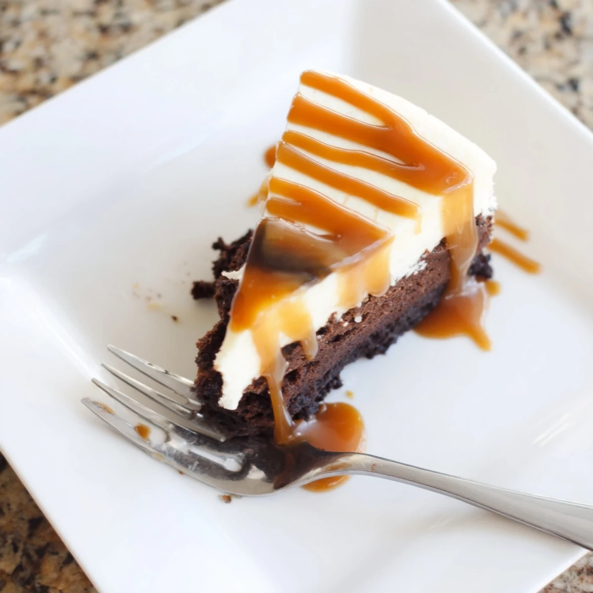 Rich caramel brownie cheesecake bliss with swirls of creamy cheesecake and luscious caramel drizzle on a white plate