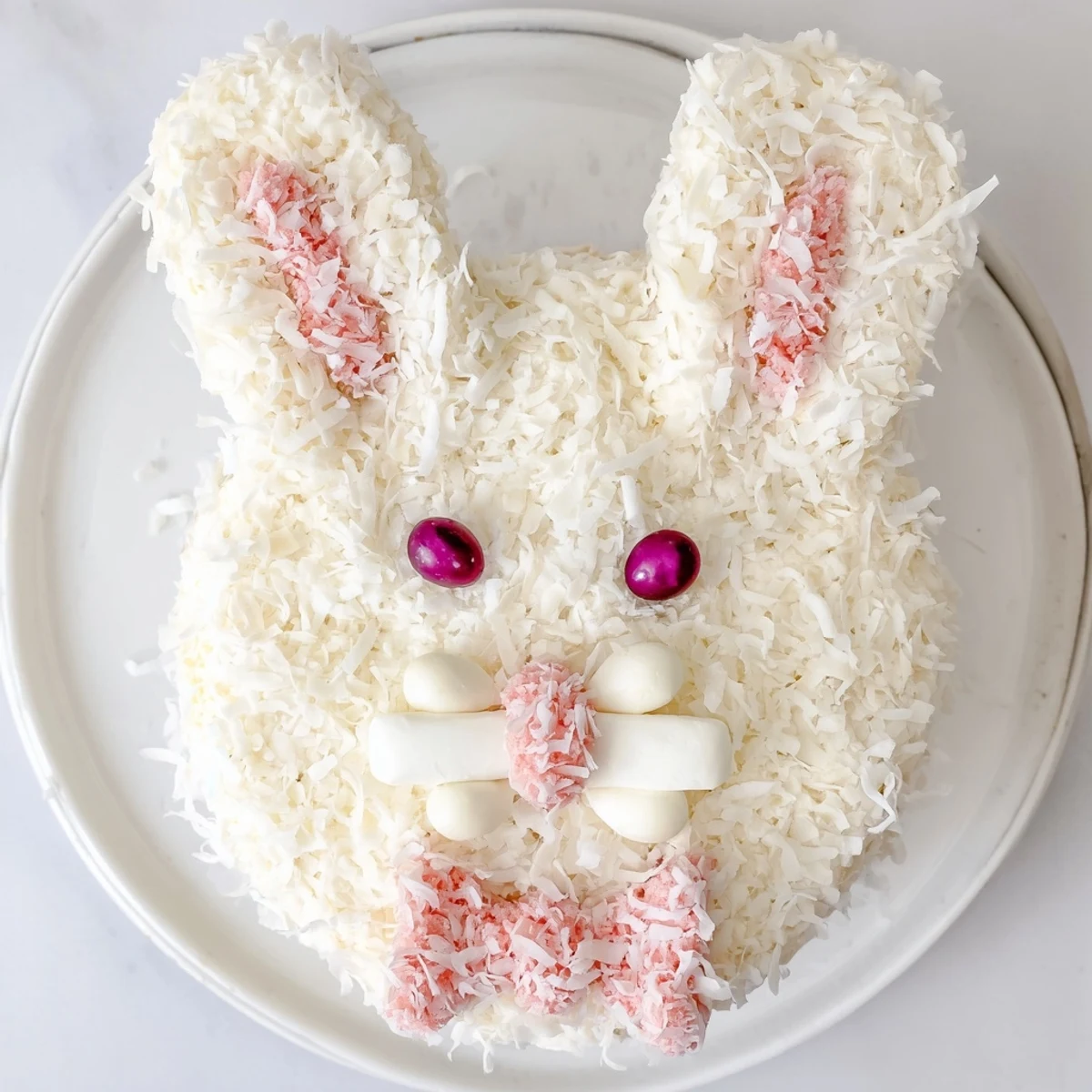 Adorable Easter bunny cake with fluffy coconut fur and pink candy details on white serving platter