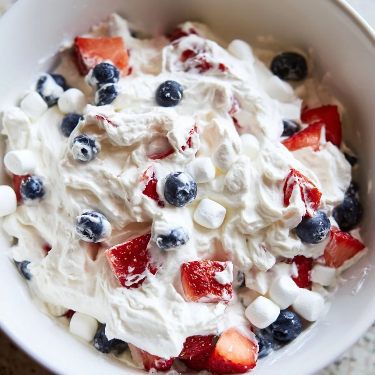 Vibrant Red White Blue Cheesecake Salad folded with fluffy marshmallows and served chilled on a summer table