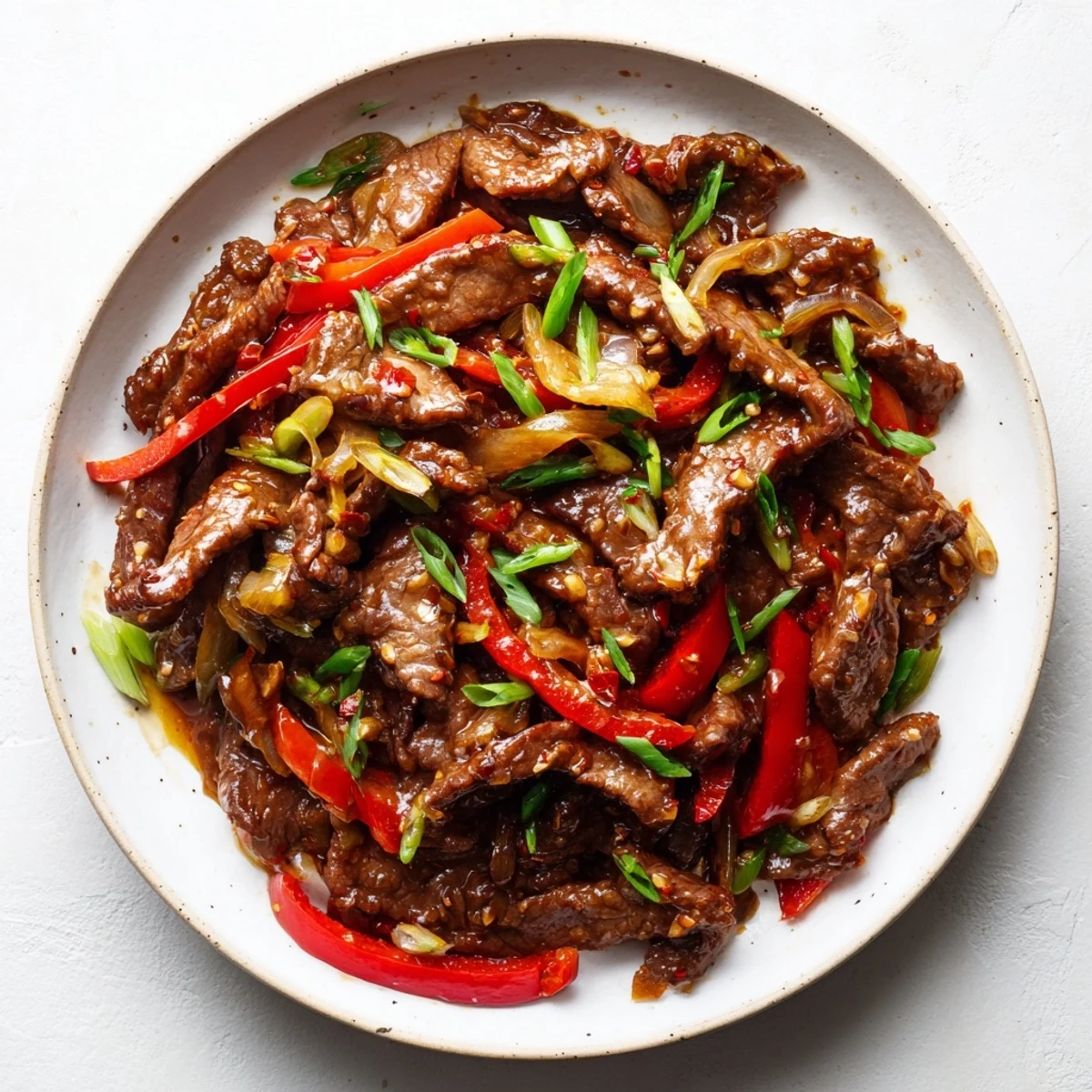 Close up of spicy beef stir fry tossed in glossy chili garlic sauce with fresh garnish