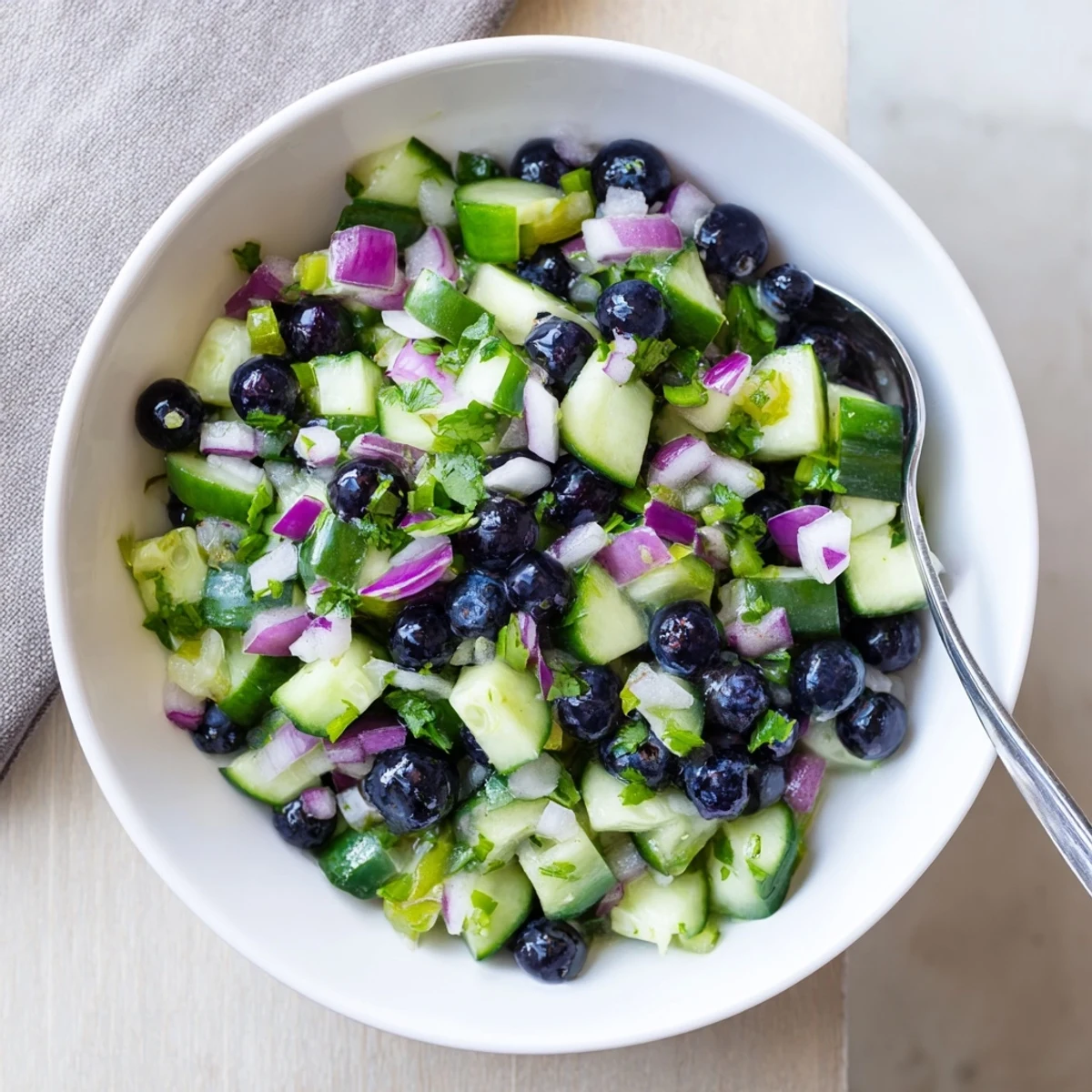 A colorful bowl of blueberry cucumber salsa with red onion, cilantro, and lime juice